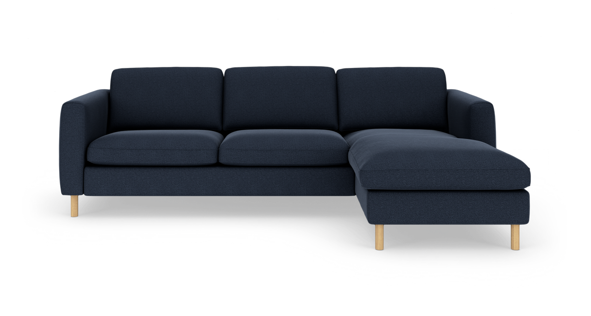 Mørkeblå hjørnesofa med chaiselong til højre og lyse træben, frilagt på hvid baggrund.