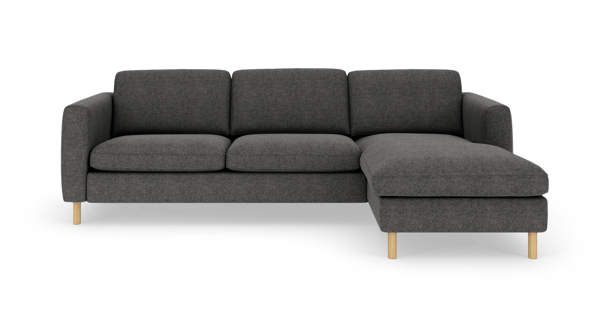 Mørkegrå tresæders hjørnesofa med chaiselong til højre og lyse træben, fritlagt på hvid baggrund.