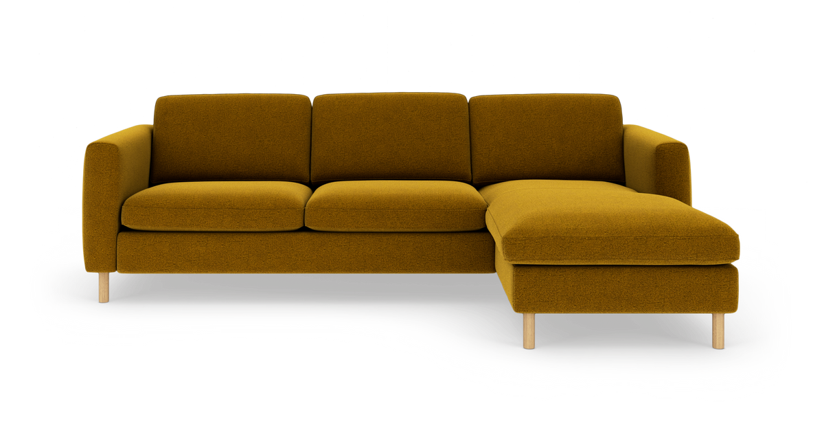 Sennepsgul hjørnesofa med chaiselong til højre, træben, tre sædehynder og rene linjer på hvid baggrund.