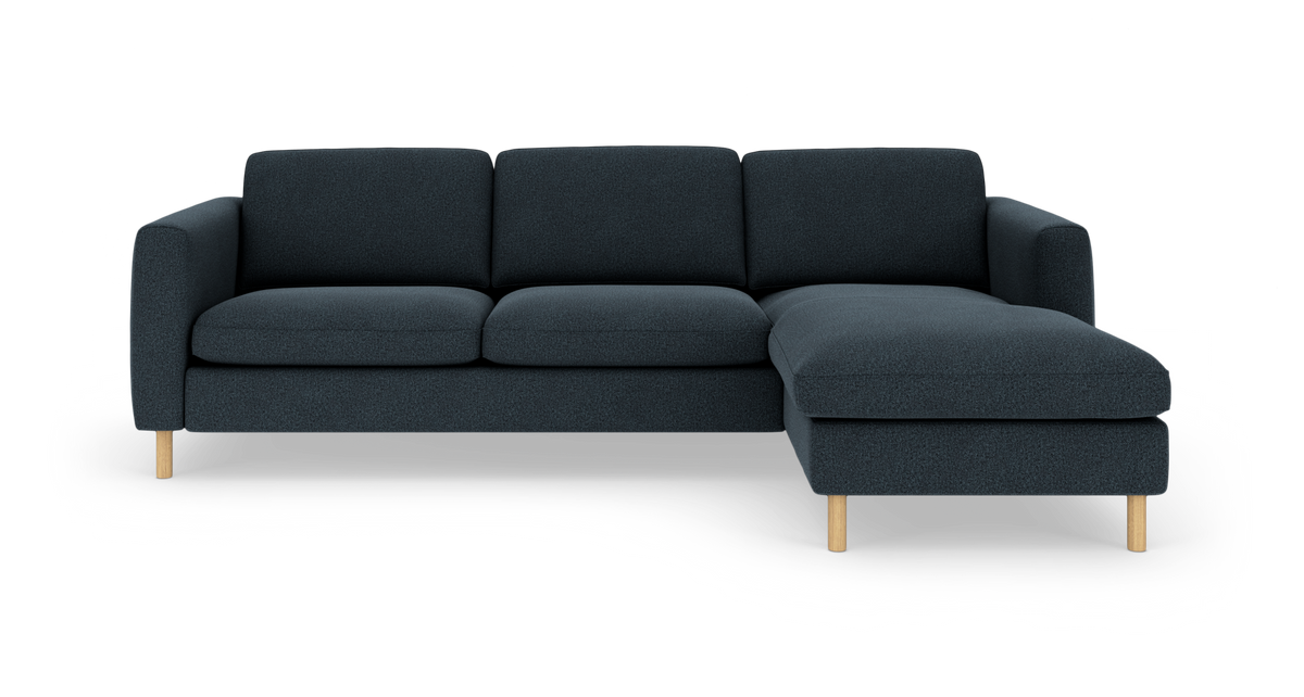 Mørkeblå hjørnesofa med højrevendt chaiselong og lyse træben, frilagt på hvid baggrund.