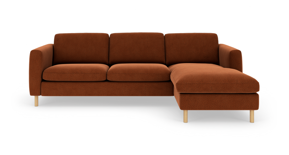 Rustfarvet tresæders sofa med chaiselong til højre og lyse træben, frilagt på hvid baggrund.
