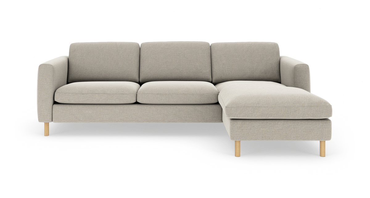 Beige hjørnesofa med chaiselong til højre, bløde sæde- og rygpuder og lyse træben på hvid baggrund.