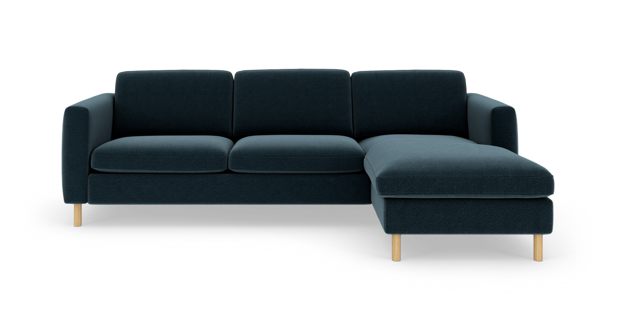 Mørk blågrøn 3-personers sofa med chaiselong til højre og lyse træben, frontvisning i studieopsætning.