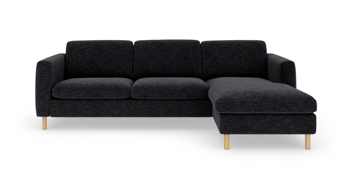 Mørkegrå hjørnesofa med chaiselong til højre og lyse træben, frilagt på hvid baggrund.