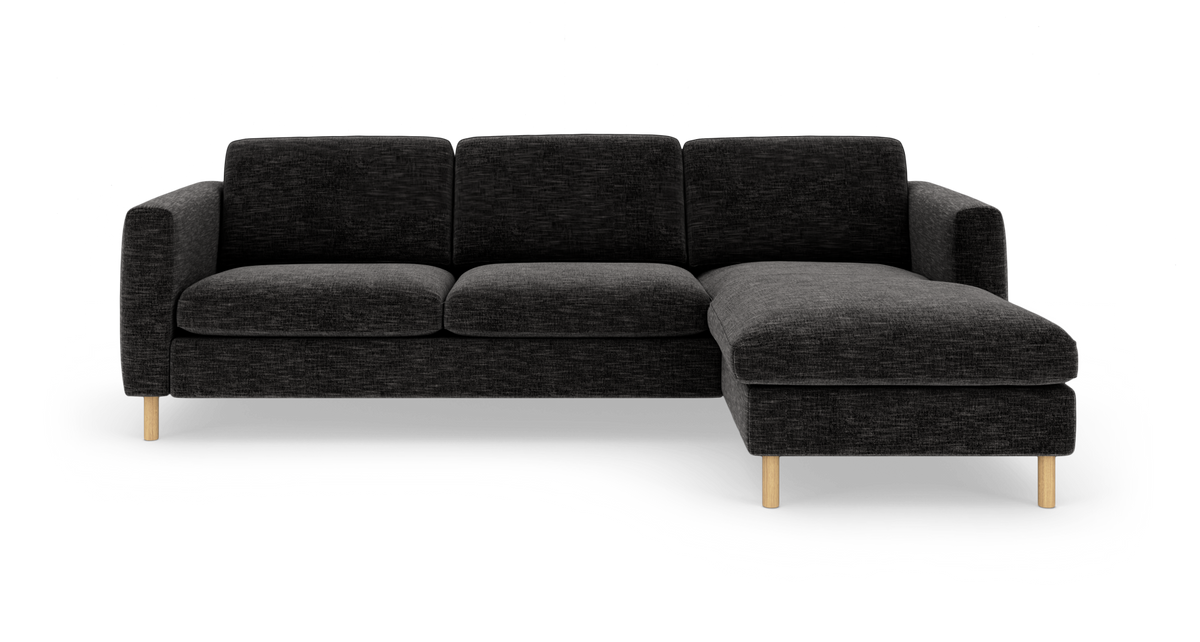 Mørkegrå hjørnesofa med chaiselong til højre på lyse træben, frilagt mod hvid baggrund.