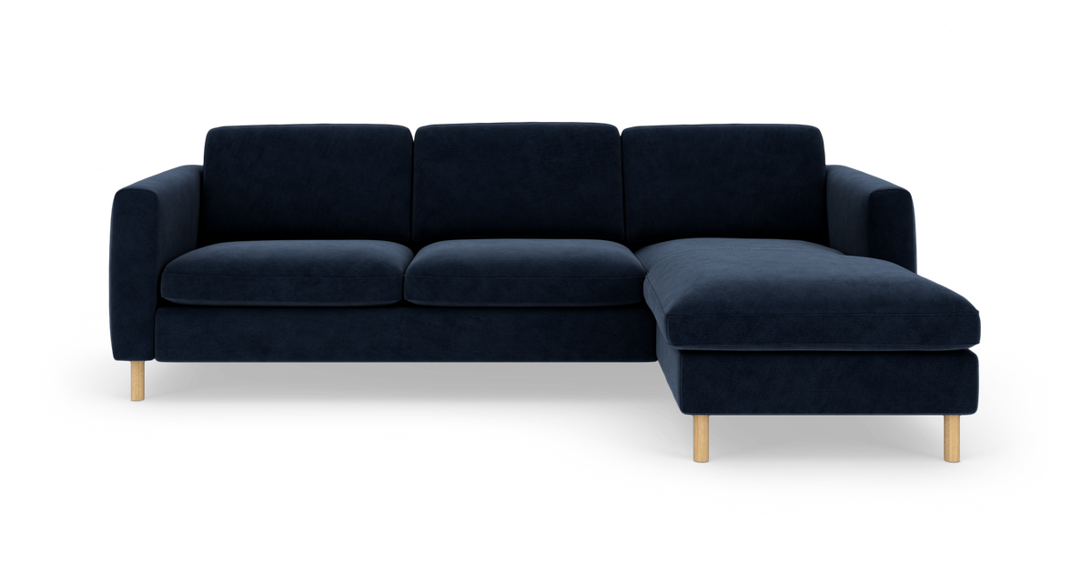 Mørkeblå hjørnesofa med højrevendt chaiselong og lyse træben, frilagt på hvid baggrund.