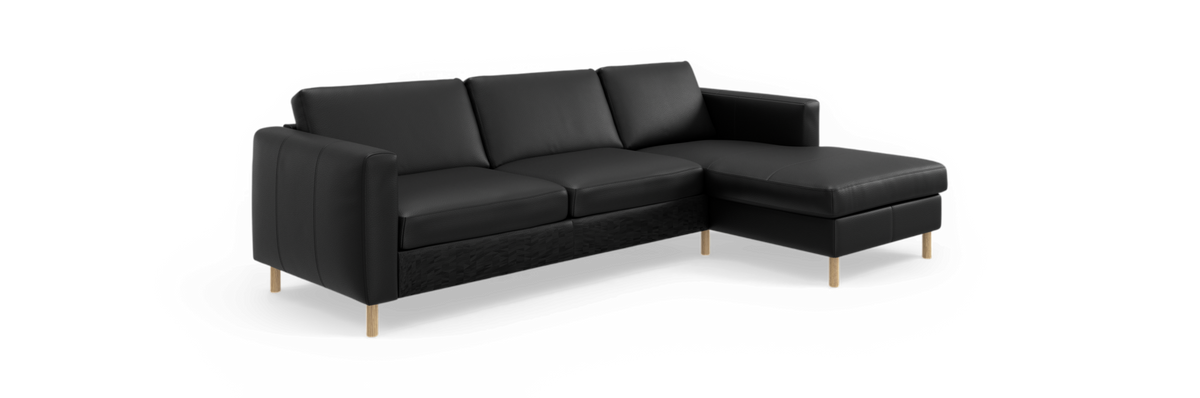 Sort hjørnesofa med chaiselong til højre og træben, isoleret mod sort baggrund.