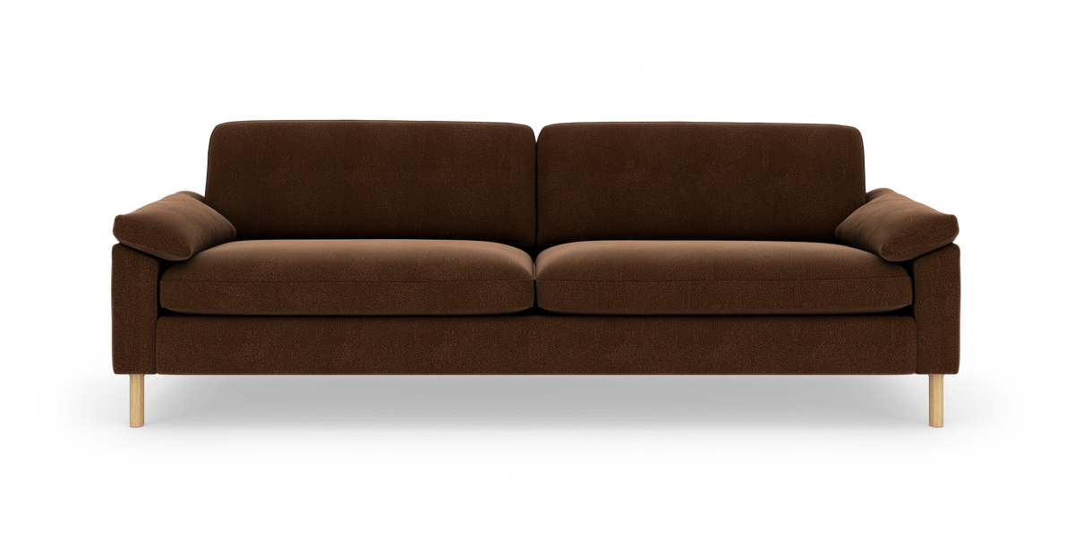 Brun 3-personers sofa med bløde puder og lyse træben, fotograferet lige forfra på hvid baggrund.