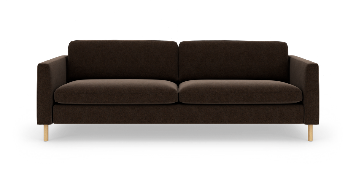 Mørkebrun 3-personers sofa med lige armlæn, to sæde- og ryghynder og lyse runde træben, fotograferet lige for i studie mod hvid baggrund.
