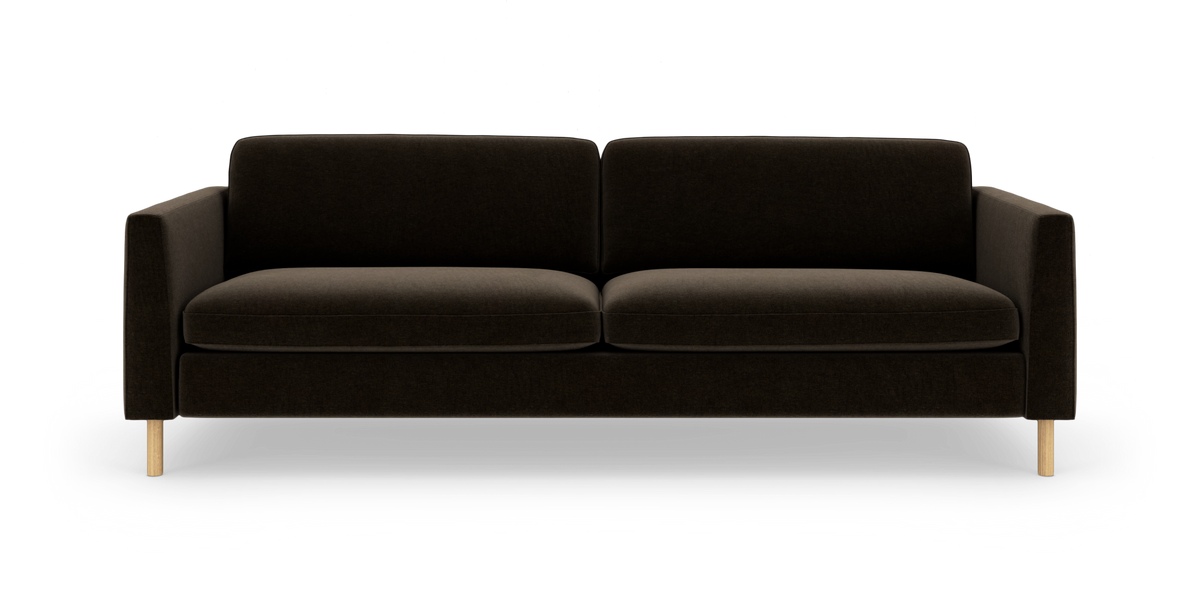 Sofa i mørkebrun polstring med lige armlæn og lyse træben, fotograferet forfra på hvid studiebaggrund.