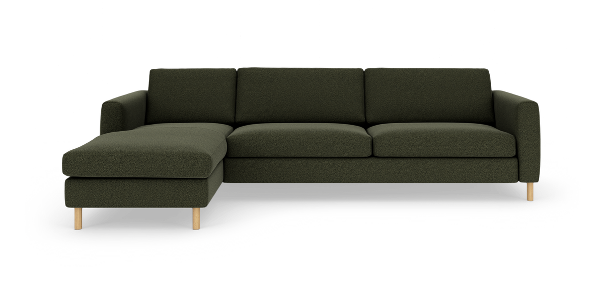 Modulsofa med venstrevendt chaiselong i mørkegrøn bouclé, runde træben, fotograferet lige for mod studiebaggrund.