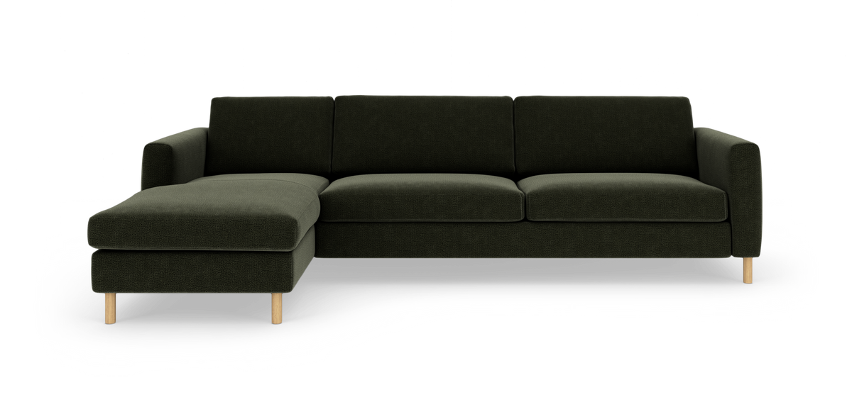 Mørkegrøn hjørnesofa med venstre chaiselong og lyse træben, frilagt på hvid baggrund.