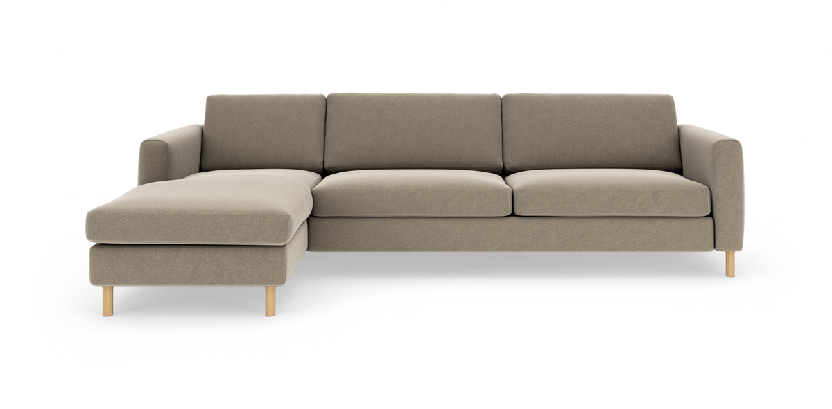Beige L‑sofa med venstre chaiselong, tre sædehynder og runde træben, fotograferet forfra på hvid baggrund.