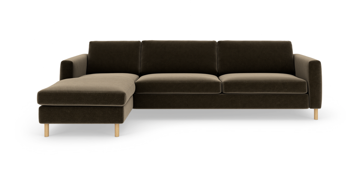 Mørkebrun hjørnesofa med venstrevendt chaiselong og lyse træben, set forfra.