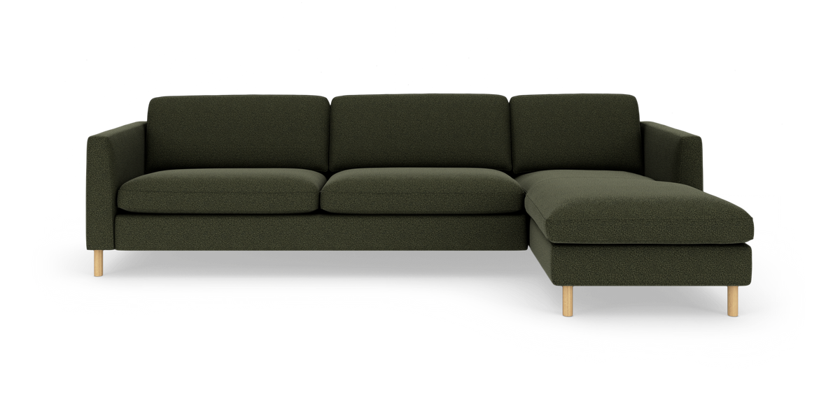 Mørkegrøn hjørnesofa med chaiselong til højre og lyse træben, frilagt på hvid baggrund.