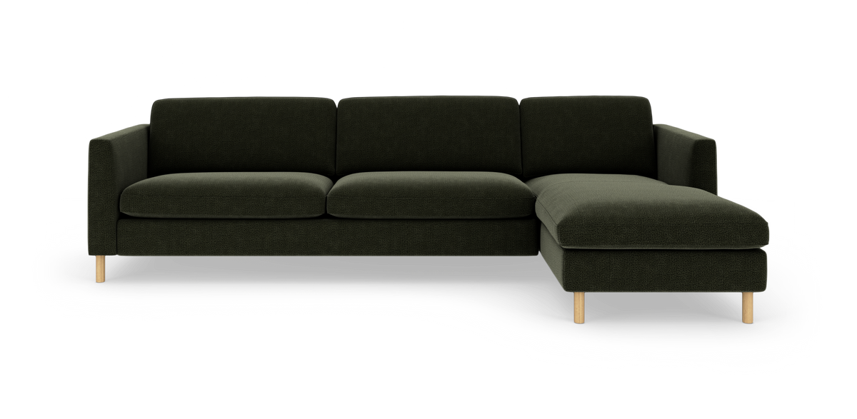 Mørkegrøn hjørnesofa med chaiselong til højre og lyse træben, fritlagt på hvid baggrund.