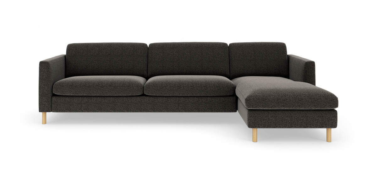 Mørkegrå hjørnesofa med chaiselong til højre og lyse træben, frilagt mod hvid baggrund.