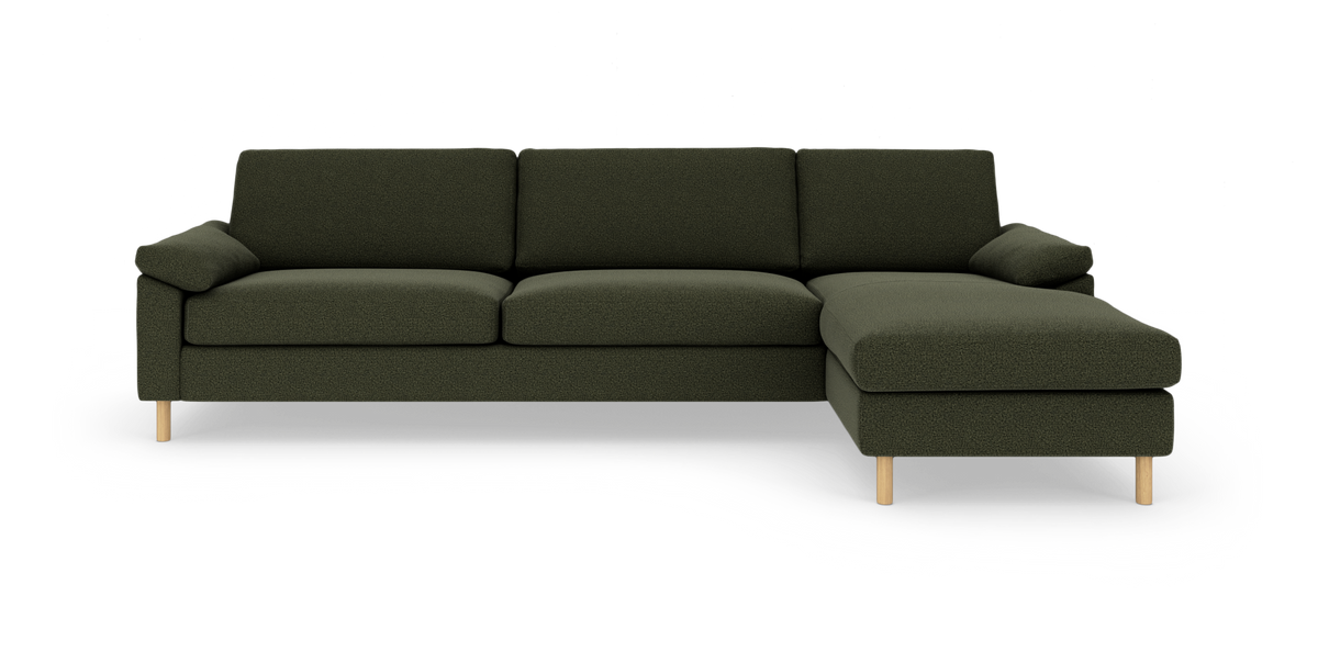 Mørkegrøn hjørnesofa med chaiselong til højre og lyse træben, frilagt på hvid baggrund.