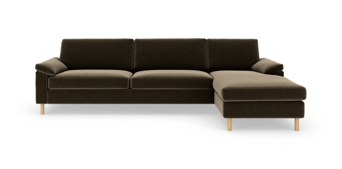 Mørkebrun hjørnesofa med chaiselong til højre og lyse træben, fotograferet lige for i studie.