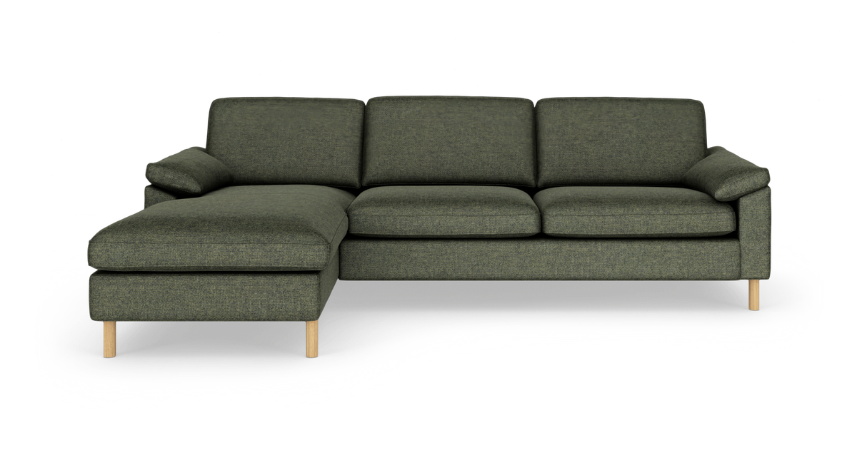 Grøn hjørnesofa med chaiselong til venstre, runde træben og bløde hynder, frilagt på hvid baggrund.