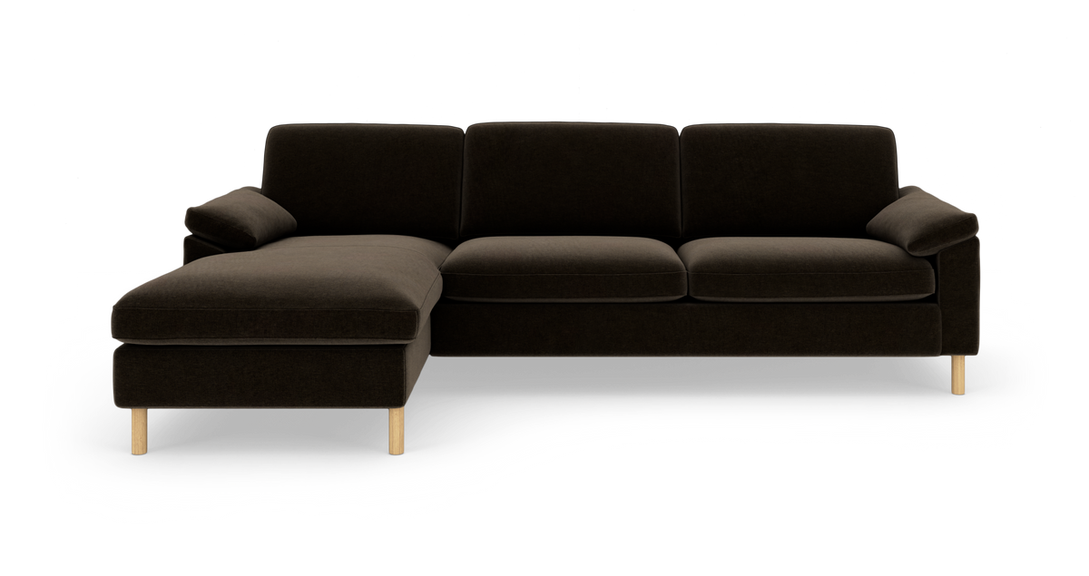 Mørkebrun hjørnesofa med venstre chaiselong og lyse træben, fotograferet lige for mod hvid baggrund.