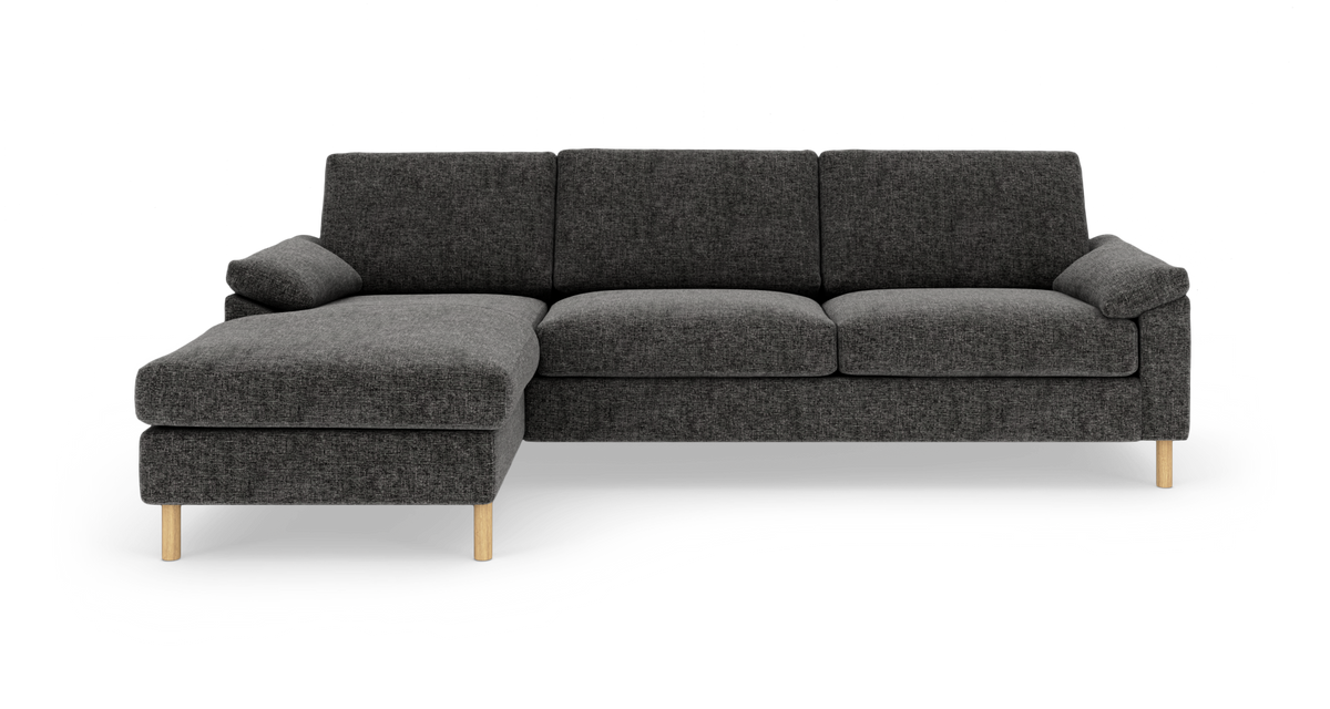 Mørkegrå L‑sofa med venstrevendt chaiselong og lyse træben, fotograferet lige for i studie.