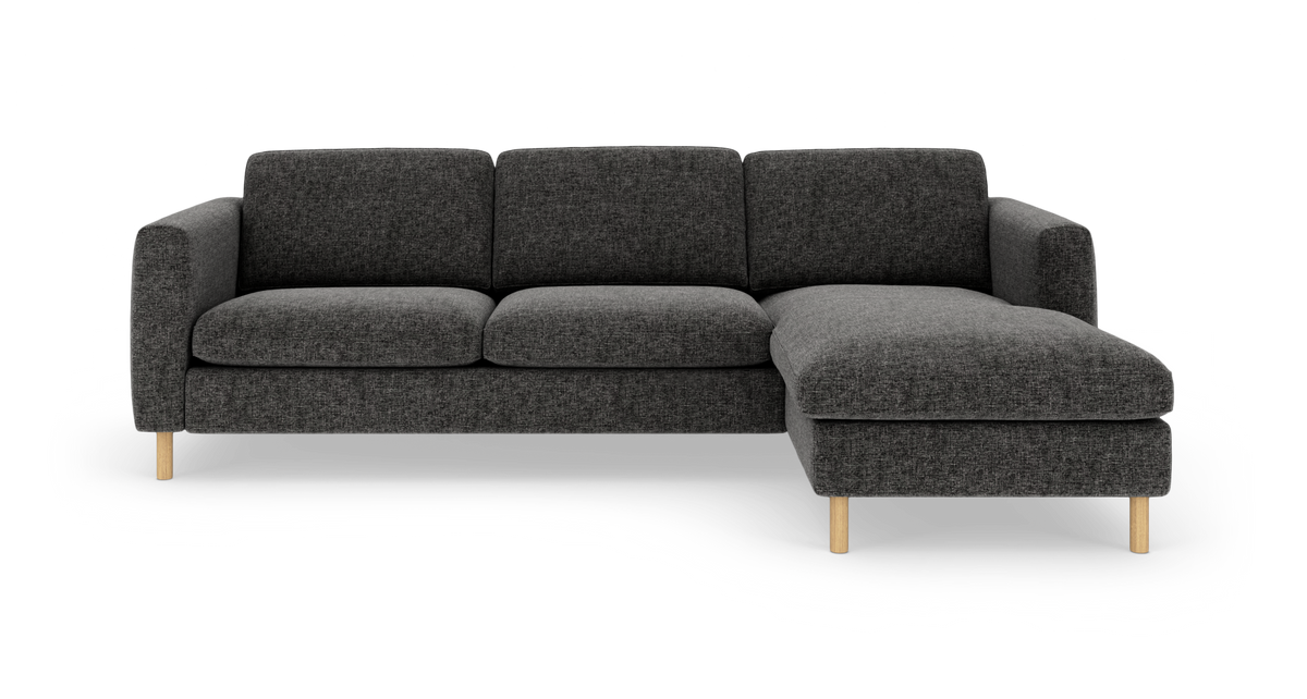 Mørkegrå 3-personers sofa med chaiselong til højre og lyse træben, set forfra på hvid baggrund.