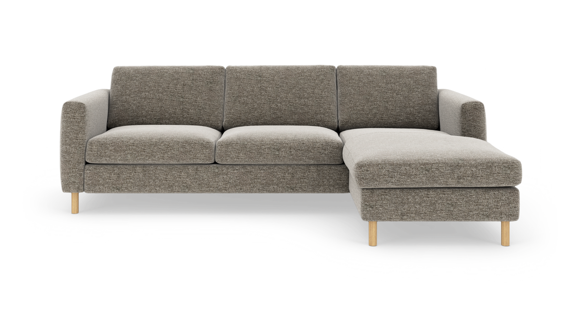 Grå hjørnesofa med chaiselong til højre og lyse træben, isoleret på hvid baggrund.