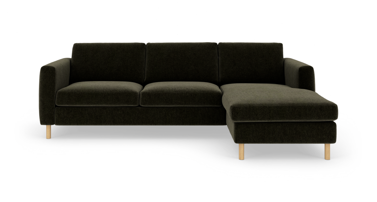 Mørkegrøn hjørnesofa med chaiselong til højre og lyse træben, frilagt på hvid baggrund.
