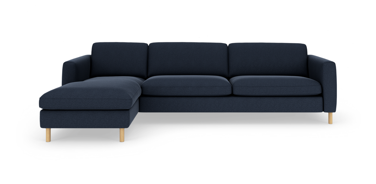 Mørkeblå hjørnesofa med venstre chaiselong og lyse træben, fotograferet lige for på hvid baggrund.