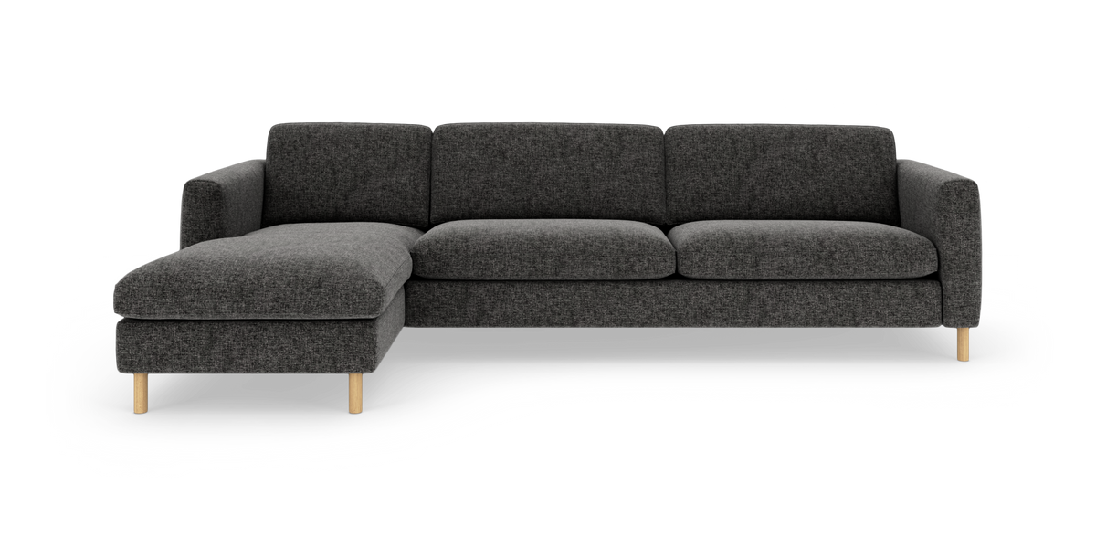 Mørkegrå hjørnesofa med venstrevendt chaiselong og lyse træben, fotograferet lige forfra på hvid baggrund.