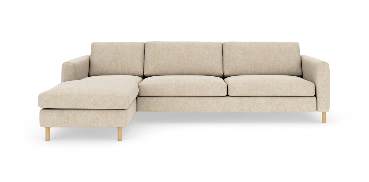Beigefarvet L‑formet sofa med venstrevendt chaiselong på træben, minimalistisk studiefremstilling.