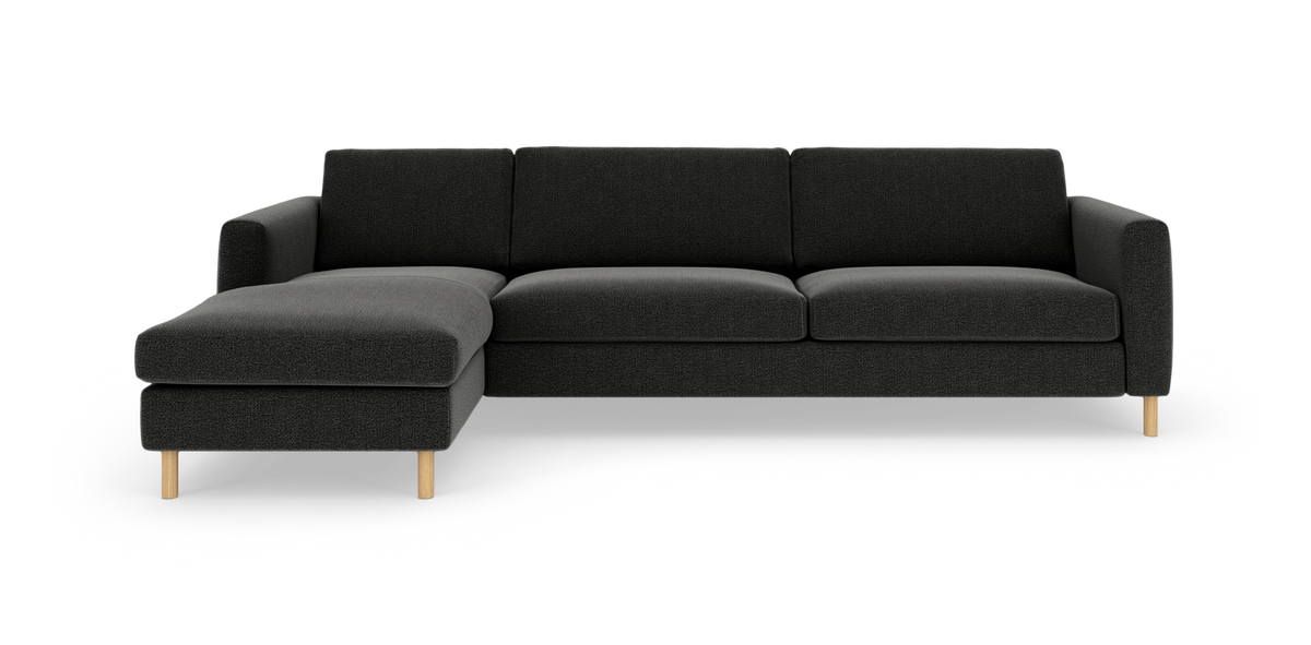 Mørkegrå hjørnesofa med chaise longue til venstre, enkle linjer og lyse træben på hvid baggrund.