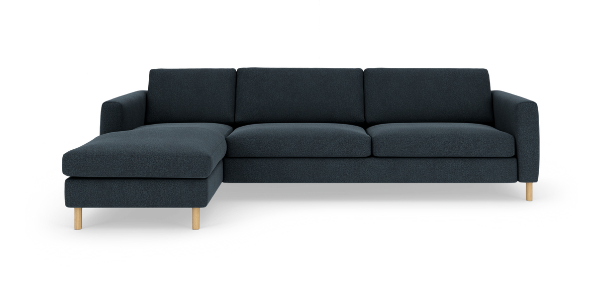Mørkeblå hjørnesofa med venstre chaiselong og lyse træben, fritlagt på hvid baggrund.