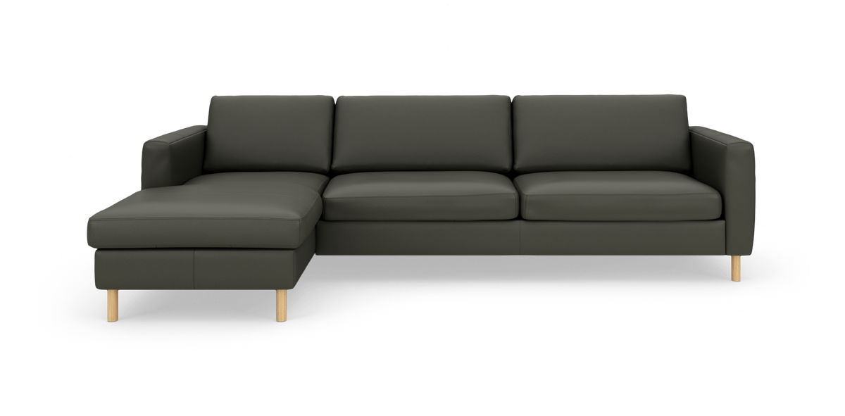 Mørkegrøn L‑sofa med venstre chaiselong og lyse træben, fritlagt på hvid baggrund.
