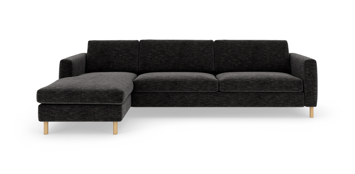 Mørkegrå hjørnesofa med venstrevendt chaiselong og lyse træben, set forfra mod hvid baggrund.