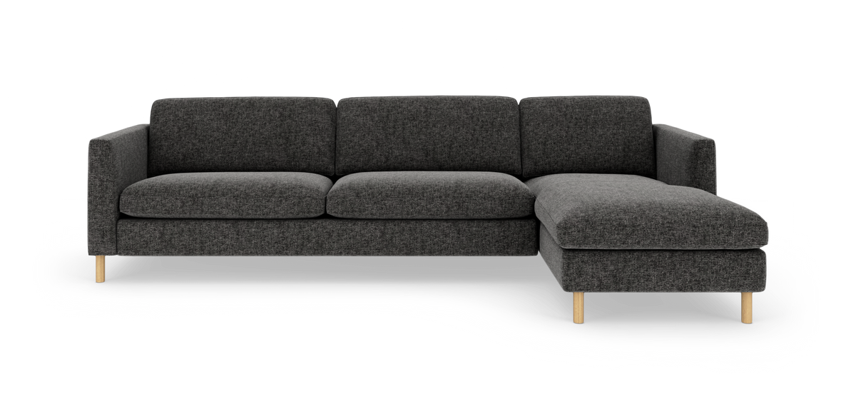 Mørkegrå hjørnesofa med chaiselong til højre på lyse træben, fritlagt på hvid baggrund.