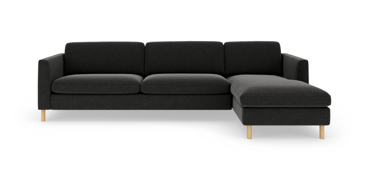 Mørkegrå hjørnesofa med chaiselong til højre og lyse træben, frilagt på hvid baggrund.