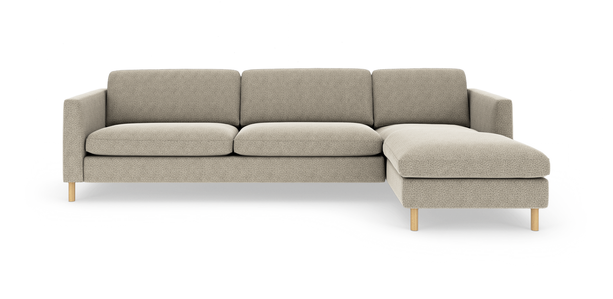 Beige hjørnesofa med chaiselong til højre på hvid baggrund, slanke træben.
