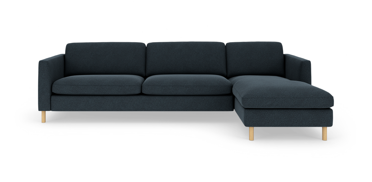 Mørkeblå hjørnesofa med chaiselong til højre og lyse træben, frilagt på hvid baggrund.