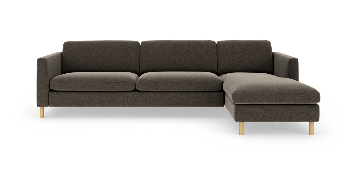 Mørkegrå hjørnesofa med chaiselong til højre og lyse træben, frilagt på hvid baggrund.