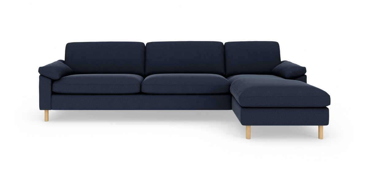 Mørkeblå hjørnesofa med chaiselong til højre og lyse træben, frilagt på hvid baggrund.
