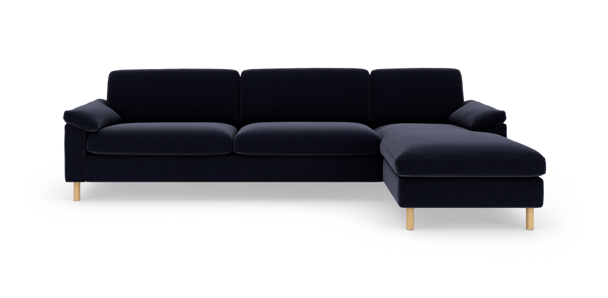 Mørkeblå hjørnesofa med chaiselong til højre og lyse træben, frilagt på hvid baggrund.