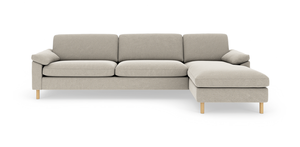 Beige hjørnesofa med chaiselong til højre, træben og bløde puder, frilagt på hvid baggrund.