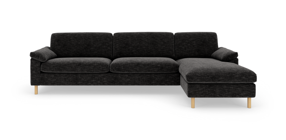 Mørkegrå hjørnesofa med chaiselong i højre side og lyse træben, frilagt på hvid baggrund.