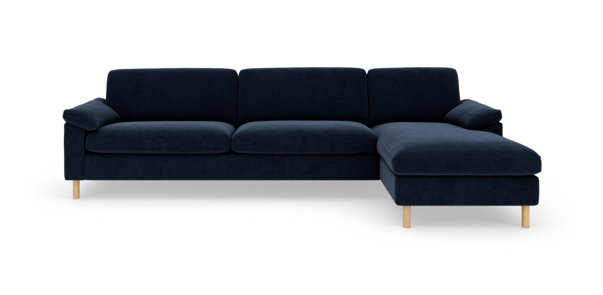 Mørkeblå hjørnesofa med chaiselong til højre og lyse træben, frilagt på hvid baggrund.