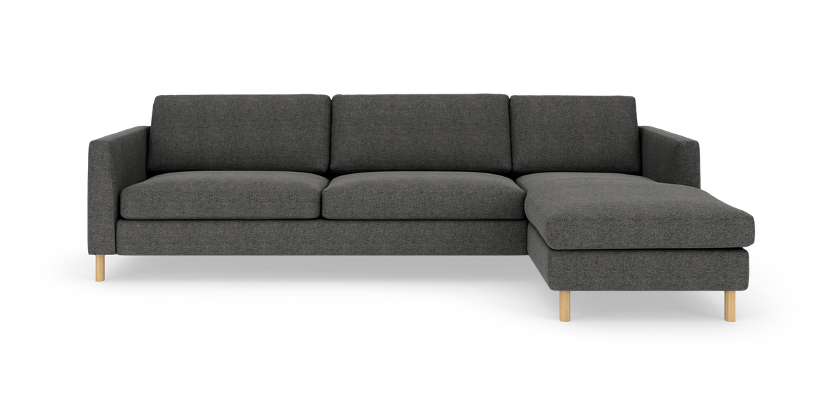 Mørkegrå hjørnesofa med chaiselong til højre og lyse træben, frilagt på hvid baggrund.