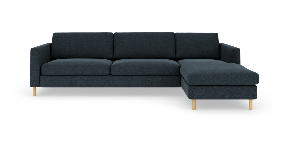 Mørkeblå hjørnesofa med chaiselong til højre og lyse træben, set forfra på hvid baggrund.