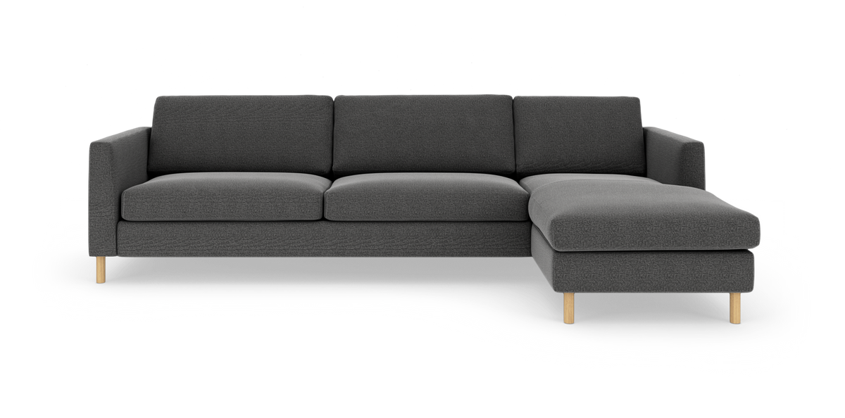 Mørkegrå hjørnesofa med chaiselong til højre og lyse træben, frontvisning på hvid studiobaggrund.
