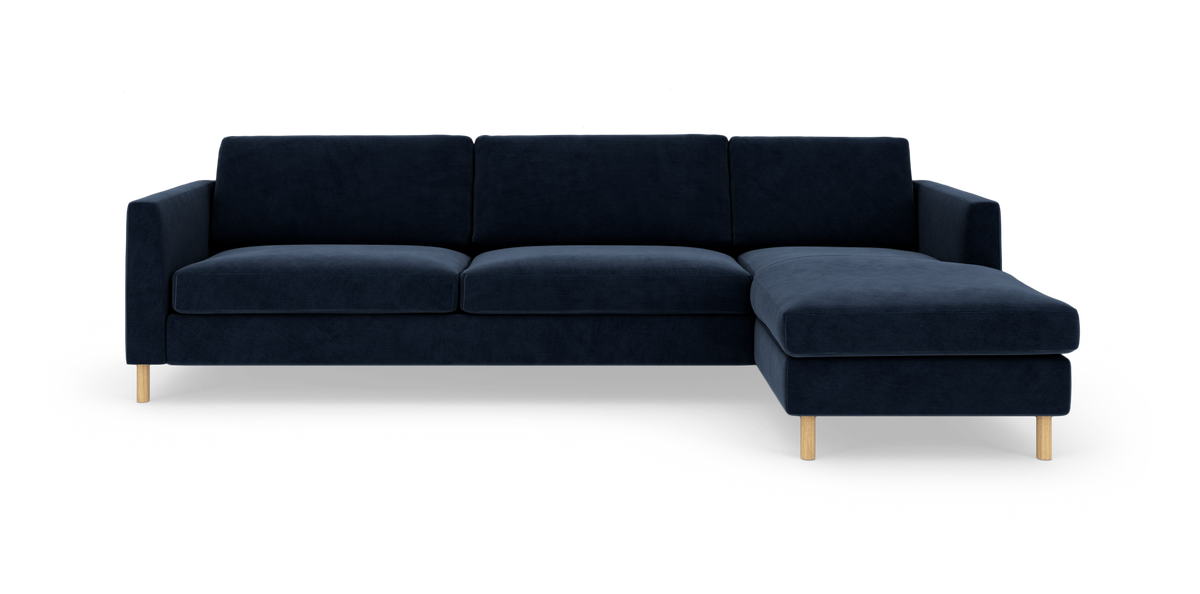 Mørkeblå modulsofa med chaiselong til højre og lyse træben, frilagt på hvid baggrund.